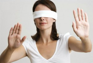 dark haired woman wearing a white blindfold holding both of her hands up in a stop gesture
